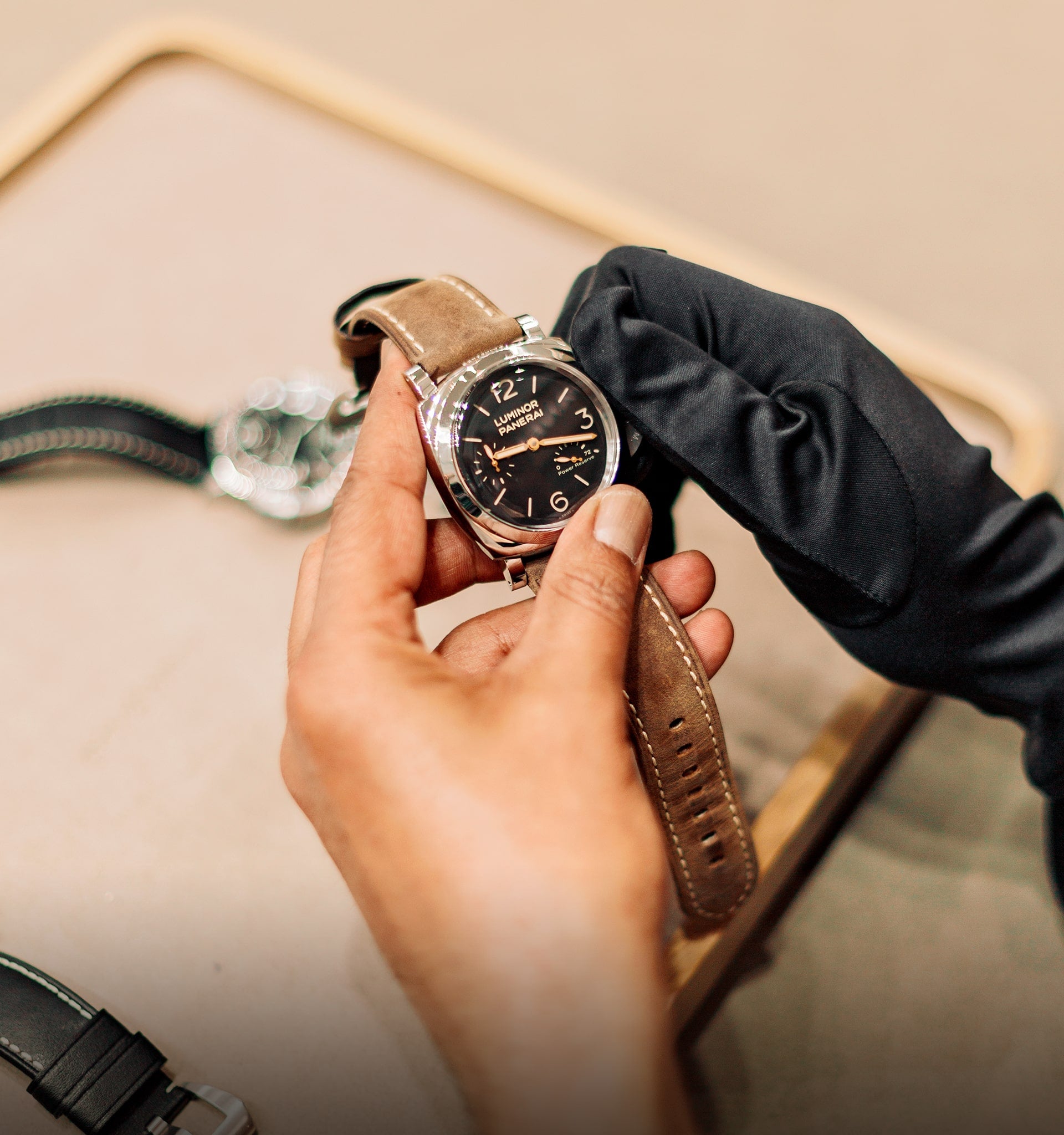Hand holding a watch with a brown leather strap against a neutral background