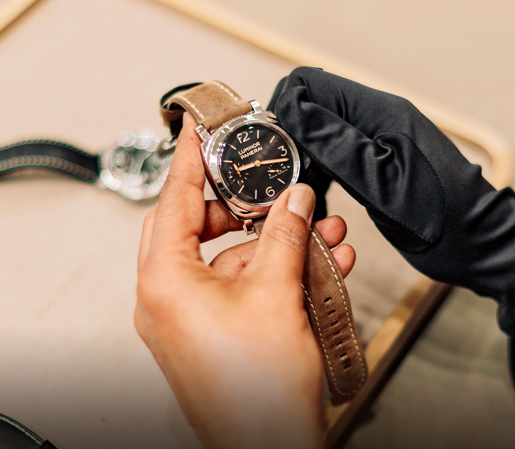 Person holding a watch with a brown leather strap, wearing a black glove.