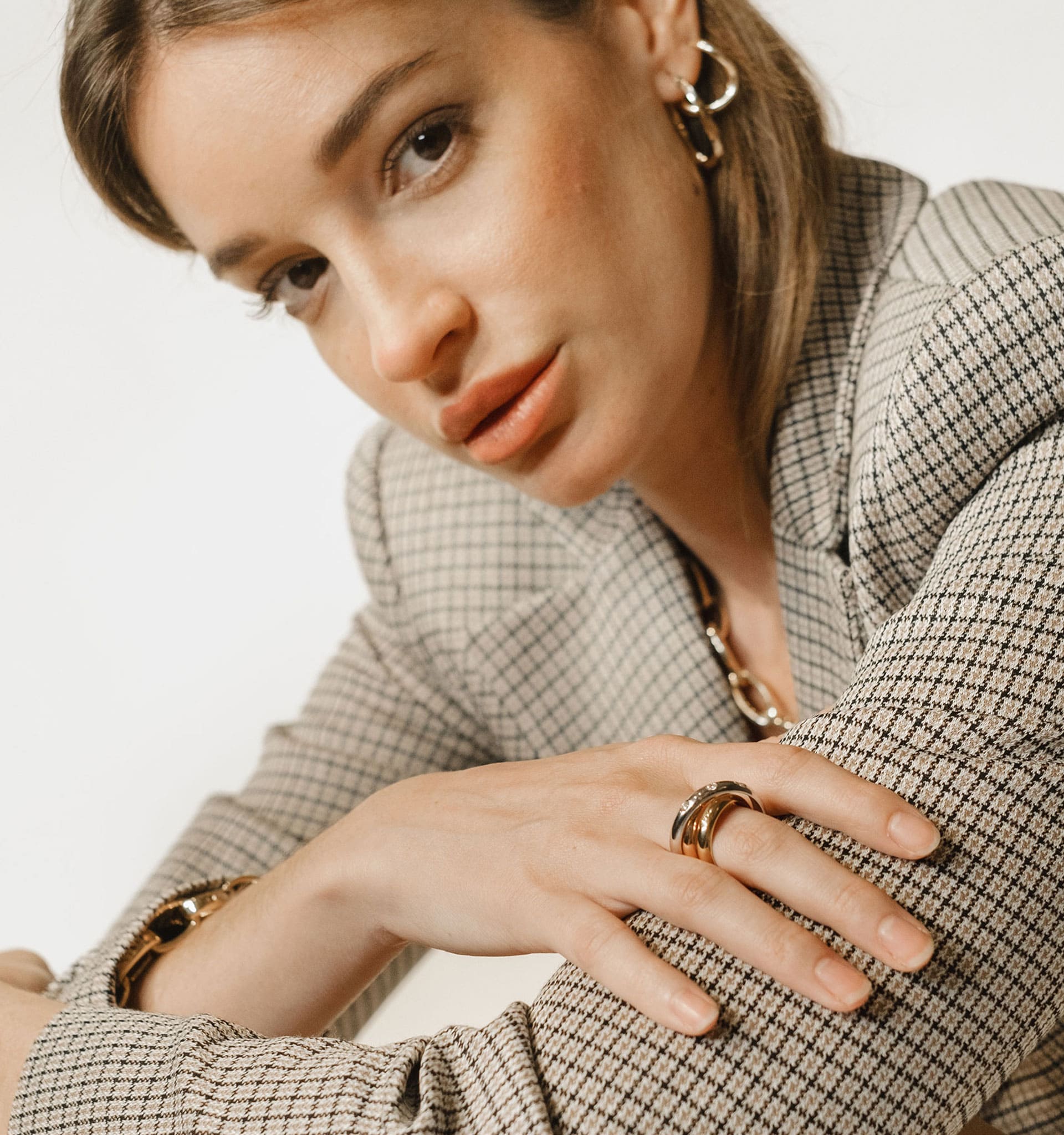 Woman wearing a checkered blazer with gold jewelry on a neutral background